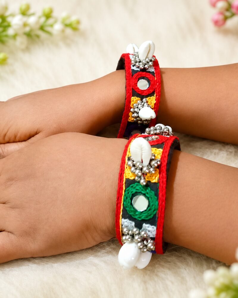 Black and red mirror-work cuffs with cowrie shell accents worn on model