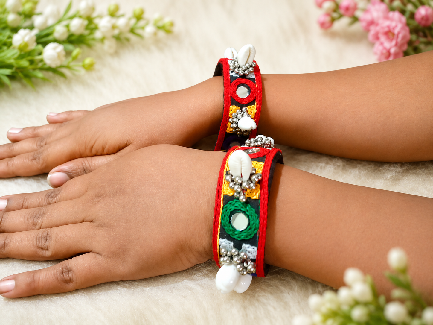 Black and red mirror-work cuffs with cowrie shell accents worn on model