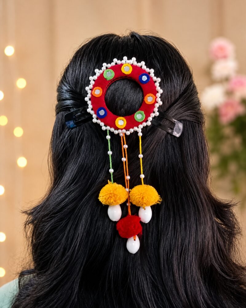 Red mirror-work hair ornament with marigold pom-poms and pearl trim
