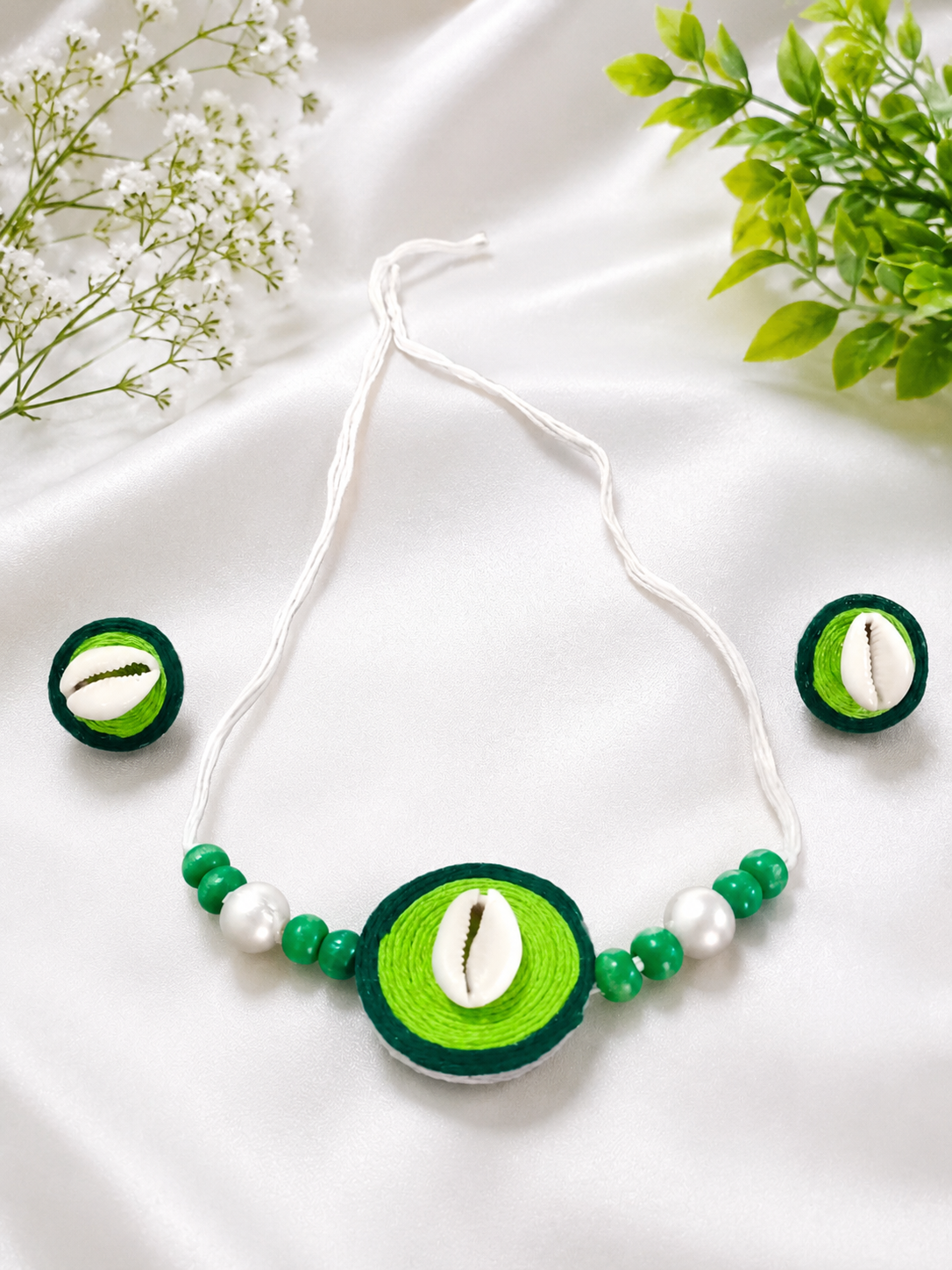 Green thread-wrapped cowrie shell necklace and earring set on white satin